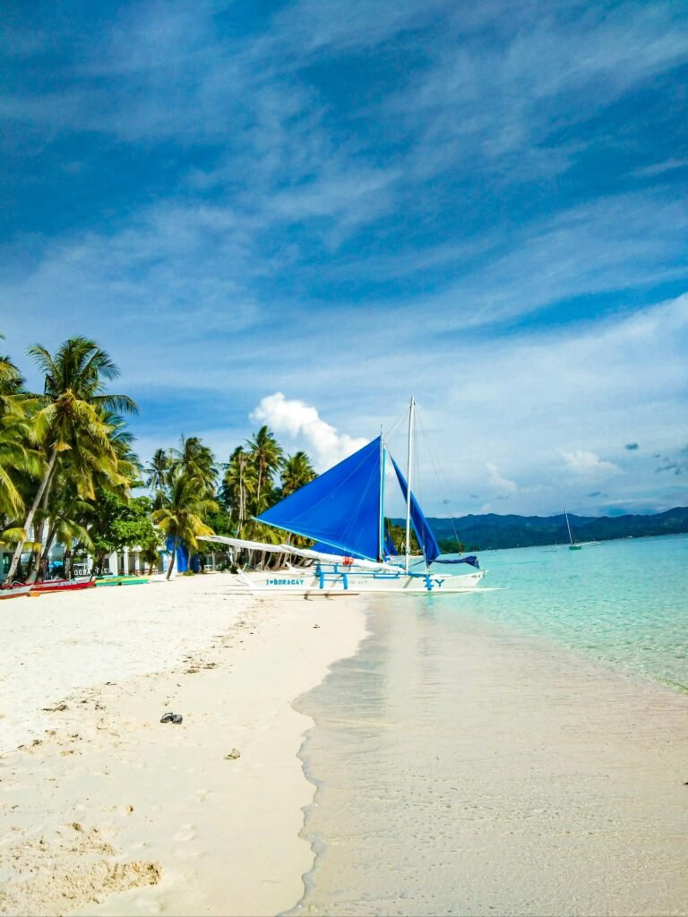 Beautiful tropical beach with palm trees and sailboat in Boracay, Philippines, under a clear blue sky.